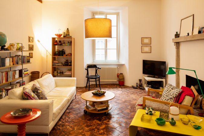 Sala de estar com piso cerâmico rústico, móveis mistos, iluminação central e decoração afetiva, evocando o vintage com personalidade.