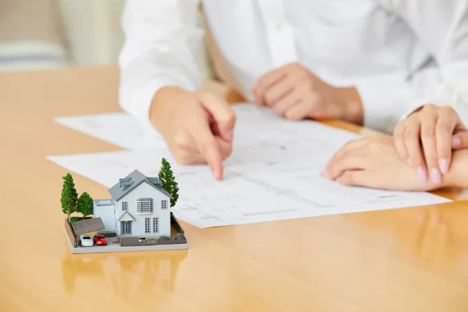 Maquete de casa sobre a mesa e pessoas analisando uma planta baixa durante uma reunião