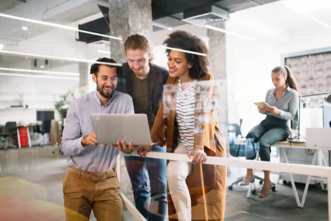 Equipe multidisciplinar interagindo com laptop em ambiente de escritório moderno e colaborativo