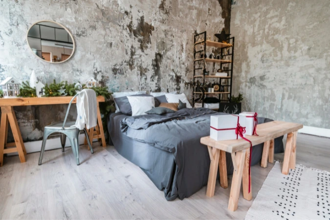 Quarto decorado com paredes descascadas, cama cinza, móveis de madeira clara e estante metálica, em ambiente industrial moderno.