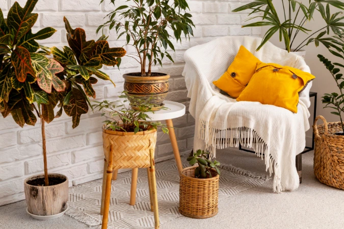 Canto de sala com poltrona boho, almofadas amarelas, manta off-white e diversas plantas em vasos de fibras naturais.