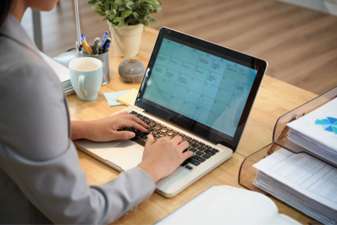 Pessoa em ambiente de trabalho utilizando o notebook com calendário digital aberto para organização de tarefas e prazos.