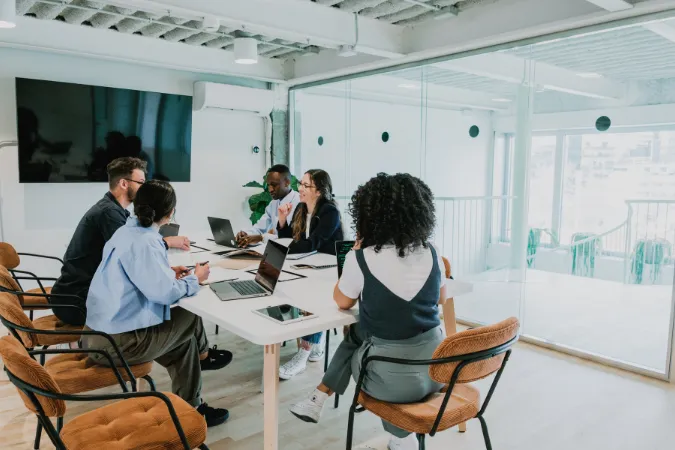 Grupo de profissionais em reunião em uma sala moderna, com laptops abertos e foco em organização de demandas e prazos.