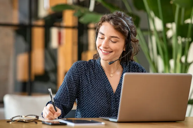 Mulher com headset anotando informações durante atendimento online