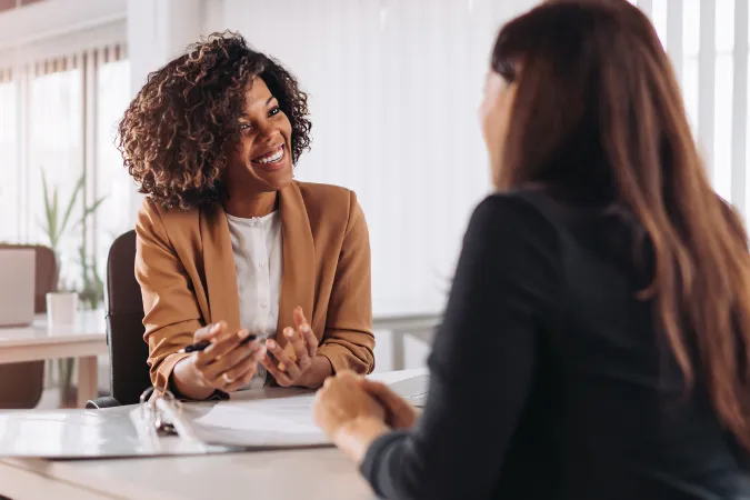 Profissional sorridente conversando com cliente em ambiente corporativo, utilizando documentos durante a reunião