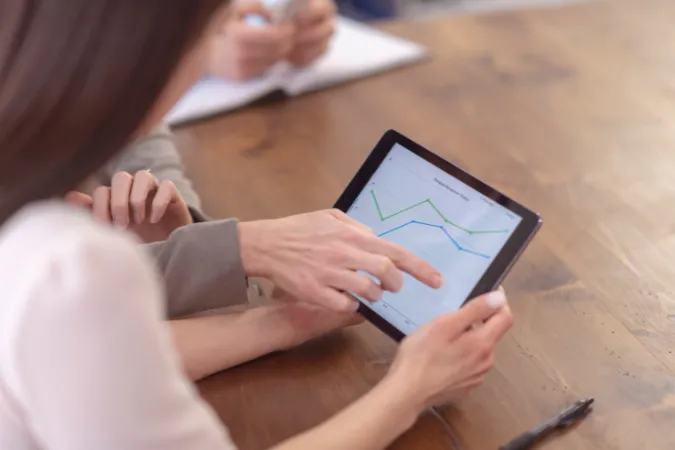 Duas pessoas analisando um gráfico de desempenho em um tablet, representando o uso de time tracking na gestão de projetos.