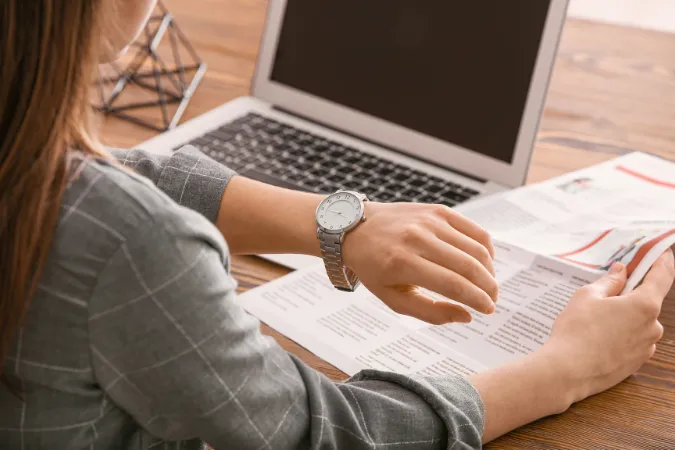Profissional conferindo o relógio enquanto analisa um relatório de tarefas, simbolizando o uso do time blocking na rotina.