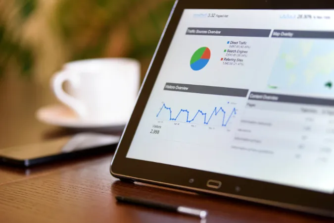 Tablet exibindo gráficos e dados analíticos de desempenho em uma mesa com xícara de café ao fundo