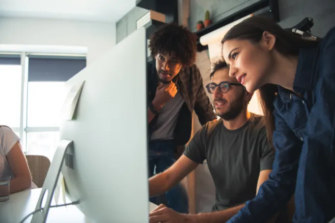 Três profissionais observando atentamente um monitor em ambiente de trabalho colaborativo