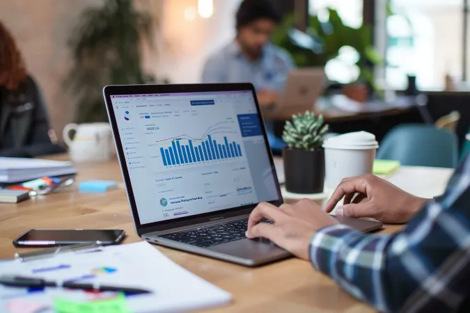 Profissional visualizando gráficos de vendas e desempenho no notebook em ambiente de trabalho colaborativo